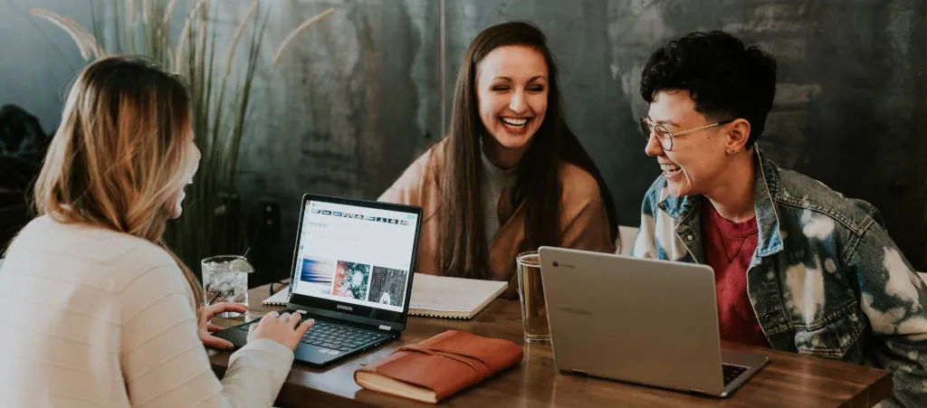 Three people sitting in front of their Notebooks in a Cafe are laughing together in relaxed working atmosphere